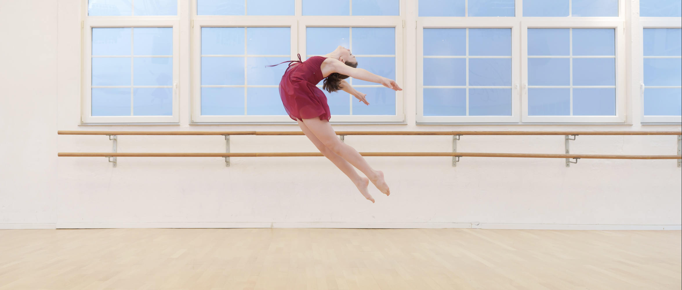 Tänzerin beim dynamischen Sprung im Tanzsaal, präzise Arm- und Beinarbeit.