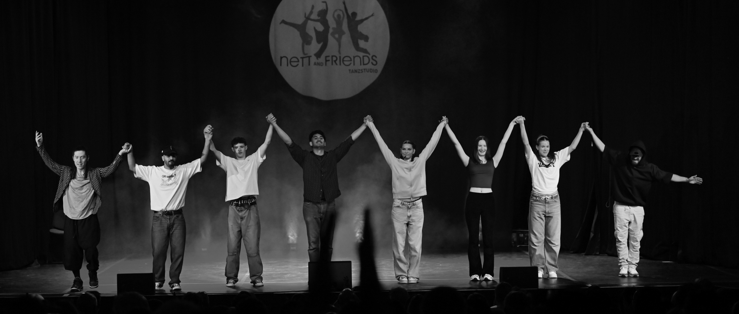 Team der Tanzschule Nett & Friends Köln und Siegburg in Schwarz-Weiß – Tänzer:innen verbeugen sich auf der Bühne nach einer Aufführung, Ausdruck von Zusammenhalt und Dankbarkeit.