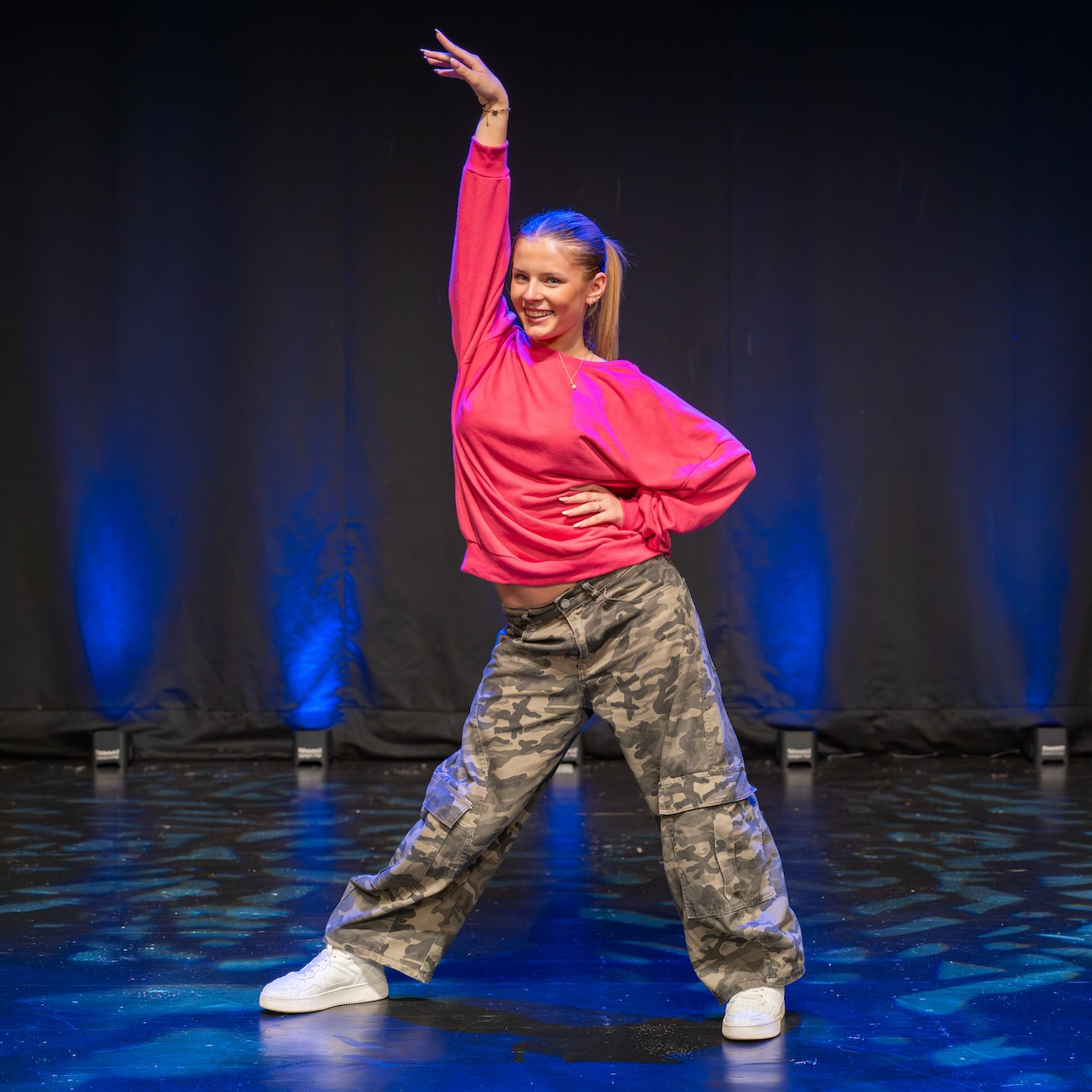 Marie in Hip-Hop-Pose auf der Bühne mit Camouflage-Hose und pinkem Oberteil