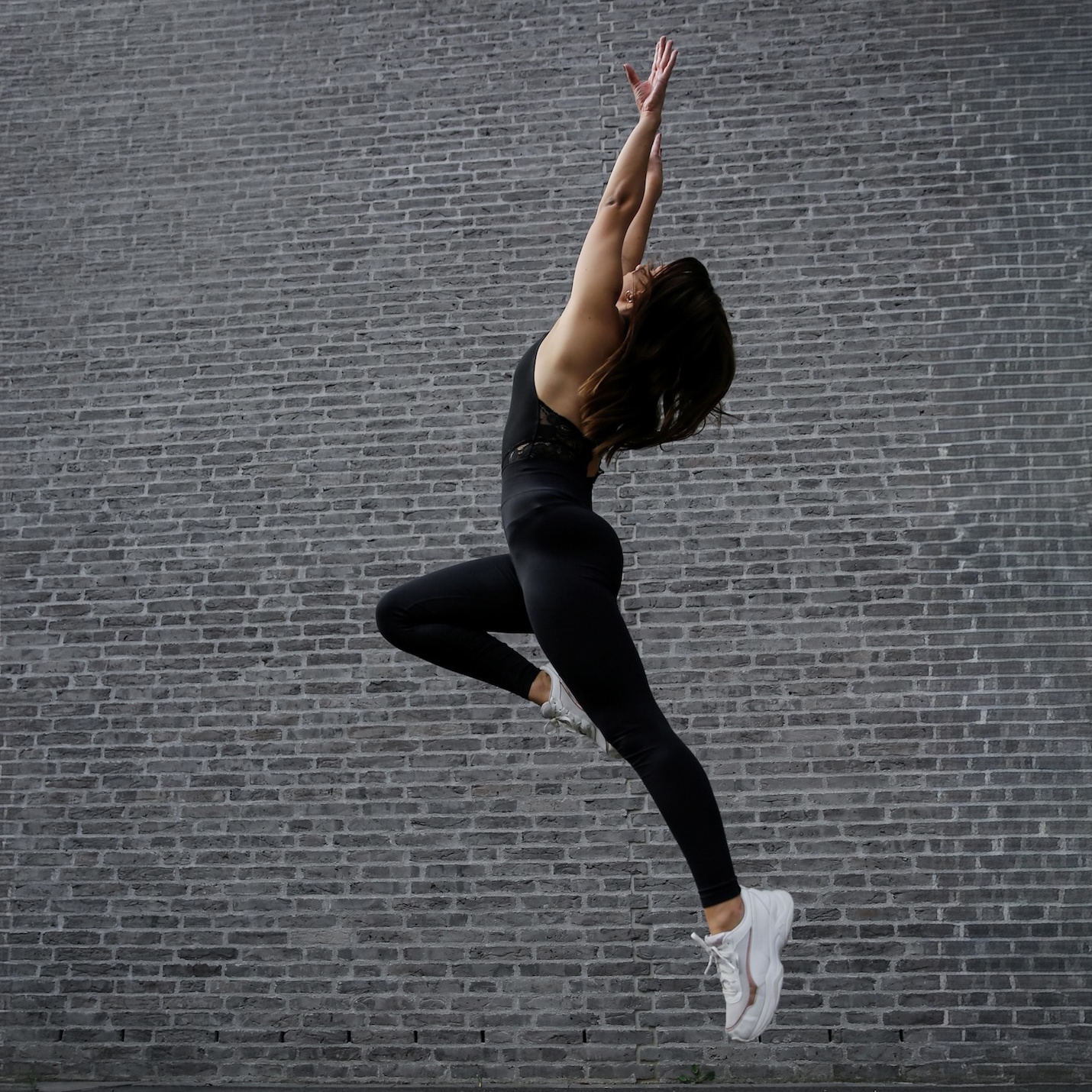 Dynamisches Tanzfoto von Vivien Aufdermauer im Sprung vor einer Mauer, schwarzer Catsuit, kraftvolle Körperspannung.